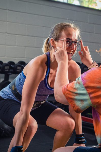 Abbie helping customer with her glasses while she lifts some heavy weights.
