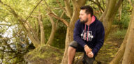 Co-Founder of Buds Fitness and Founder Of Together We Lift Sat in a tree, in his Navy Mental Health Hoodie looking out on a restful lake in Cambridgeshire