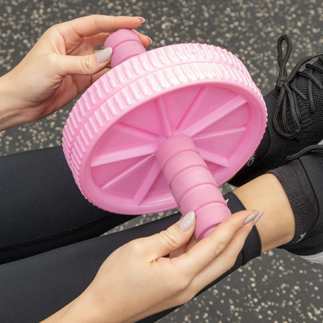Person holding a pink ab roller with dual wheels and foam handles while preparing for a core workout.