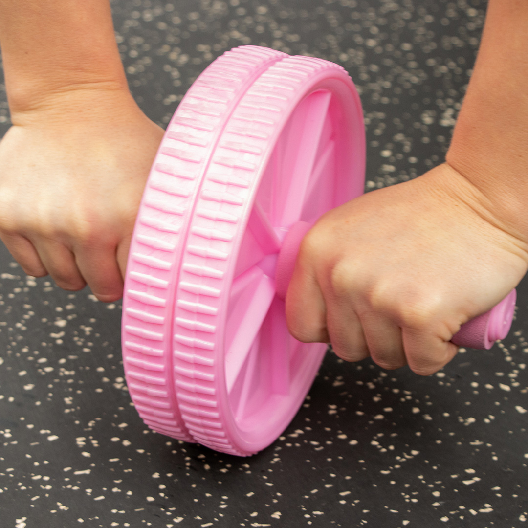 Pink dual-wheel ab roller being used on gym flooring during a controlled abdominal rollout exercise.