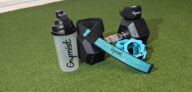 Affordable Gym Accessories including Gymist shaker bottle, lifting straps, and teal barbell collars on turf.