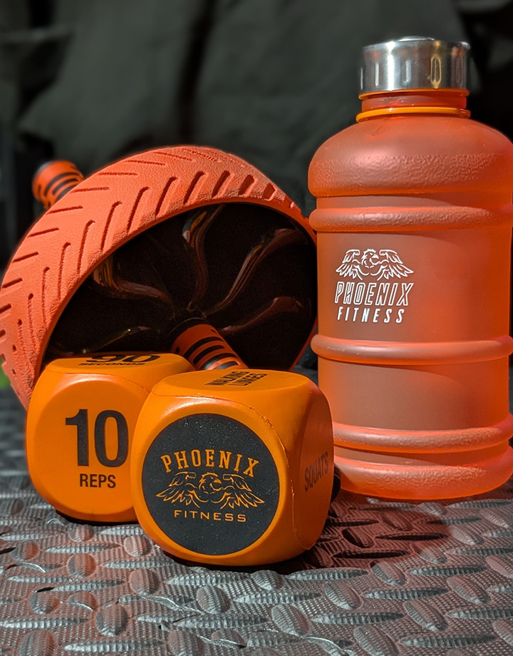 Phoenix Fitness orange exercise dice, ab roller, and water bottle on a gym floor in Cambridgeshire.