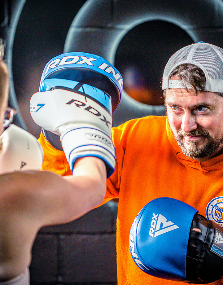 Coach Liam holding RDX boxing focus mitts during a training session, featuring blue and white RDX gloves available at Buds Fitness in Cambridgeshire.